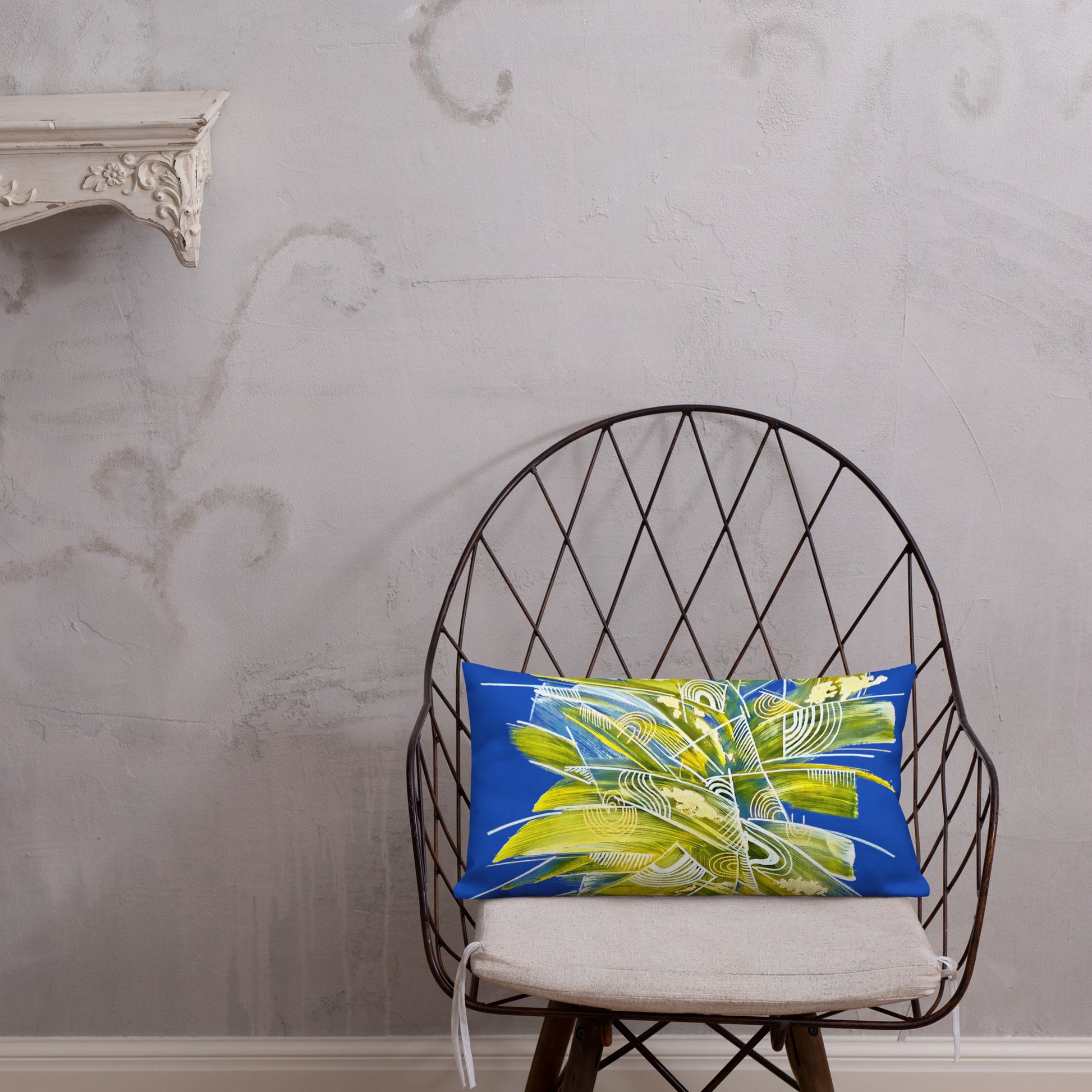 Decorative artistic blue pillow with a leaf pattern on a wire chair against a textured wall.