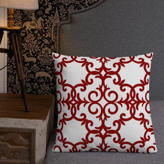 A square-shaped throw pillow with a red geometric pattern on a white background, placed on a gray surface next to a ornate lamp and a patterned wall.